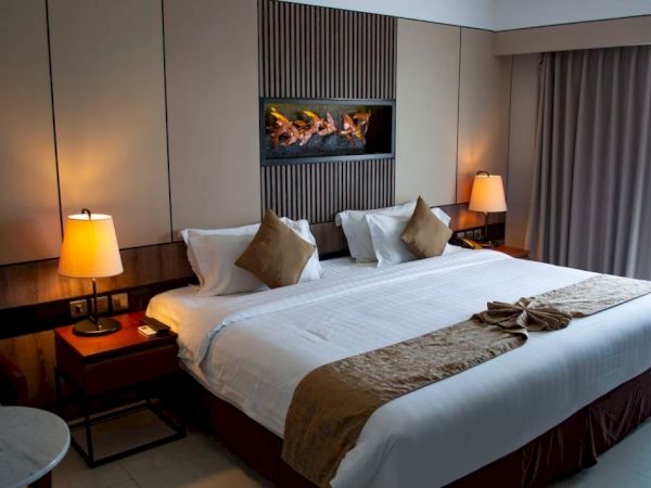 A neatly made hotel room features a large bed with pillows, bedside tables with lamps, and a wall decoration above the bed.