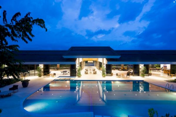 A luxurious, well-lit building at night with a large swimming pool reflecting the structure under a vibrant blue sky ends the sentence.
