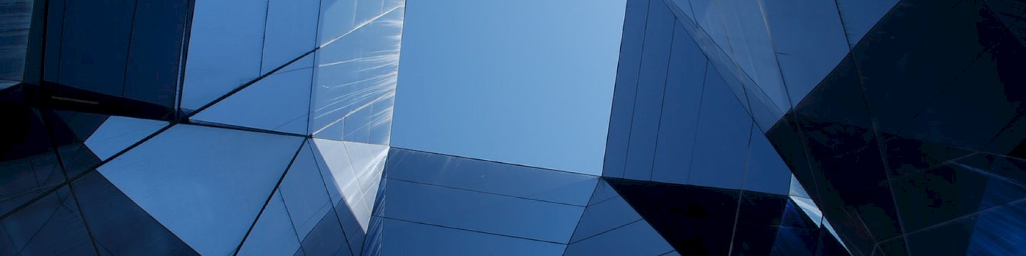 Geometric architectural structures form a polygonal opening against a blue sky, highlighting reflections and modern design aesthetics.