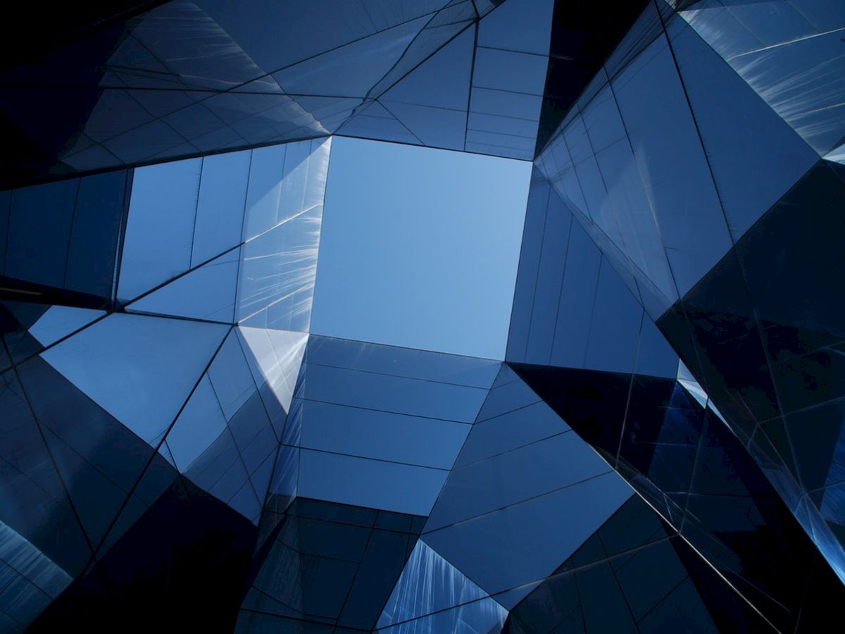The image shows a geometric architectural structure with reflective glass panels forming a pattern around a clear blue sky.