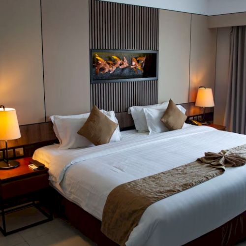 A cozy hotel room with a large bed, decorative pillows, bedside lamps, and elegant wall art, creating a comfortable and inviting atmosphere.