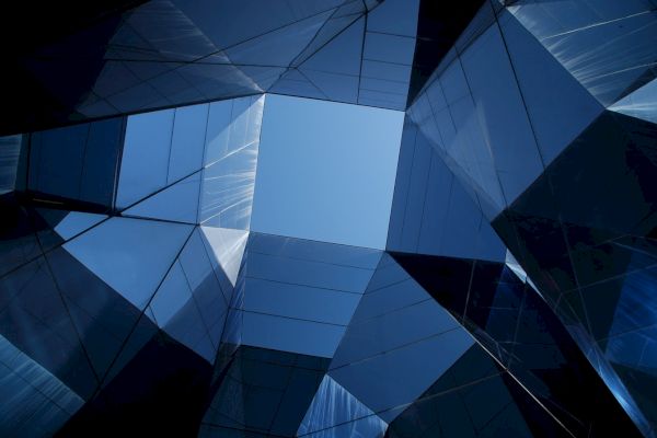 The image shows a view looking up at a geometric structure with mirrored surfaces reflecting the sky in the center.