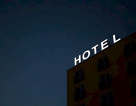 A building with a "HOTEL" sign is shown against a dark sky, with some rooms visible.
