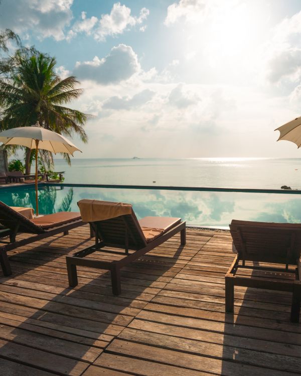 A serene poolside scene with lounge chairs, umbrellas, and palm trees overlooking a tranquil ocean under a sunny sky.