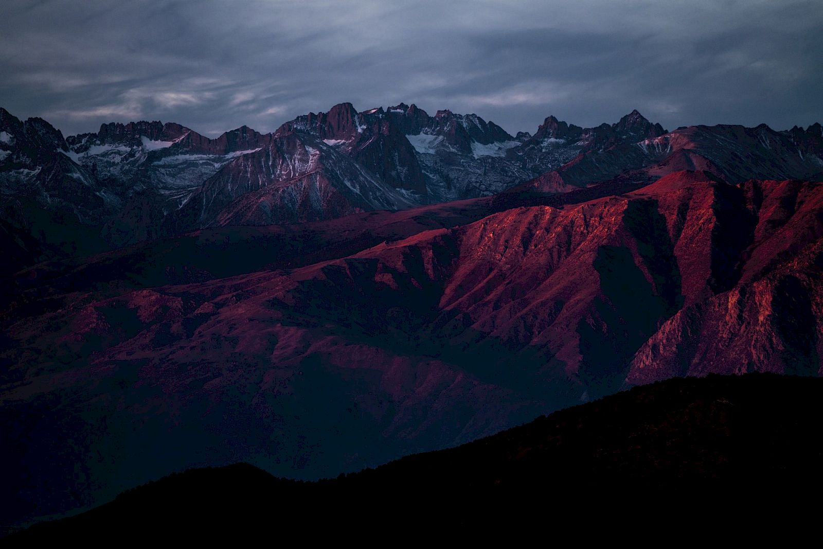 A mountain range illuminated by a dramatic, reddish sunset under a cloudy sky.