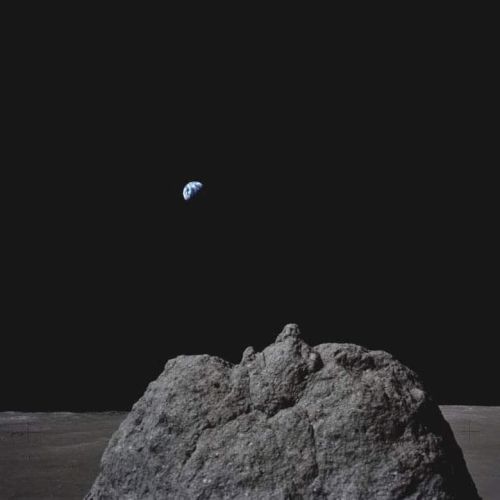 A rocky lunar surface with a view of Earth in the distant black sky, creating a striking space scene.