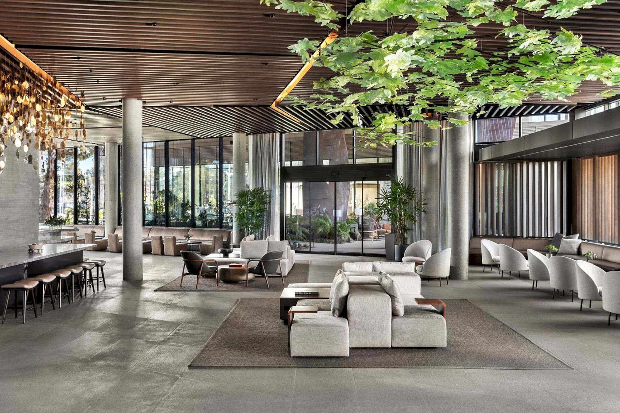 Modern lobby with stylish furniture, green leafy decor, and large windows for natural light. Seating areas create an inviting atmosphere.