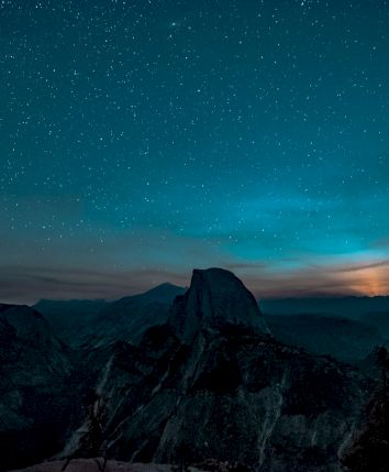 A starry night sky over a mountainous landscape, with a prominent peak silhouetted against the horizon.