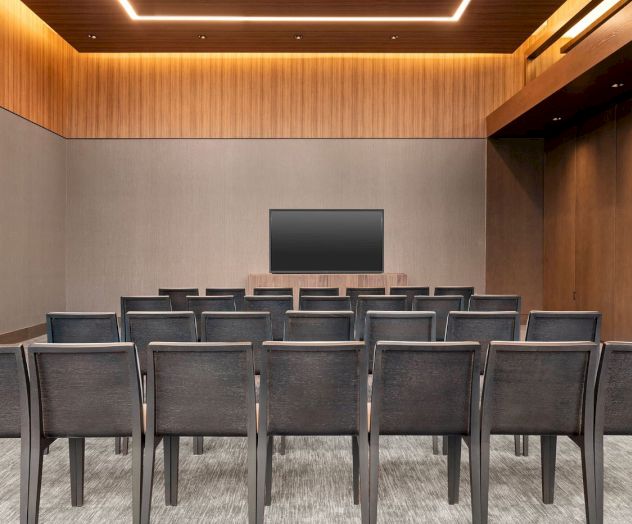 A small conference or meeting room with rows of chairs facing a screen, decorated with wood paneling.