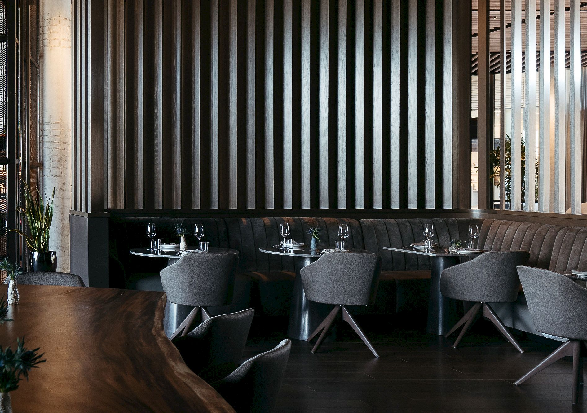 A modern restaurant interior with grey chairs, set tables with glasses, and a wooden divider.