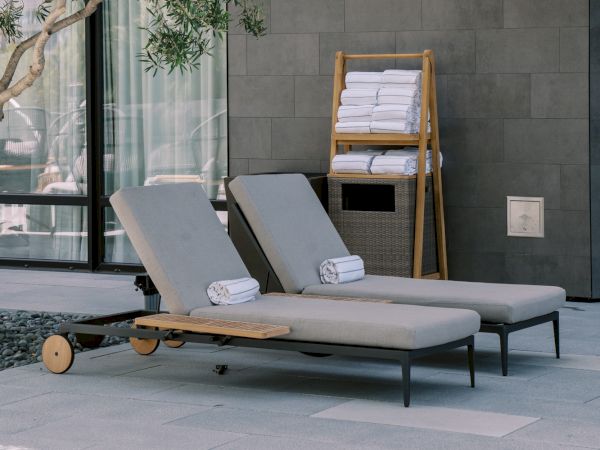 Two outdoor loungers with towels beside a modern building, surrounded by trees under natural light.