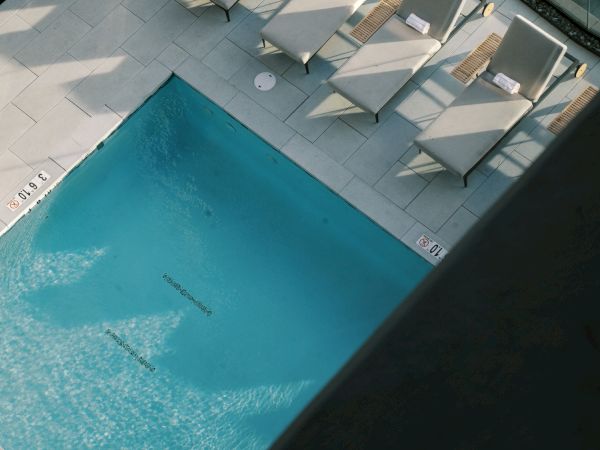 Aerial view of a pool area with lounge chairs aligned beside it, surrounded by potted plants and glass railings.