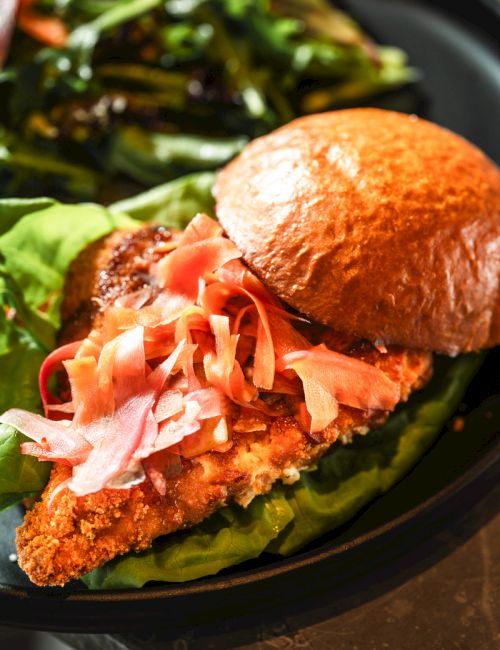A breaded sandwich cutlet topped with shredded ham, lettuce, and a roll on a plate.