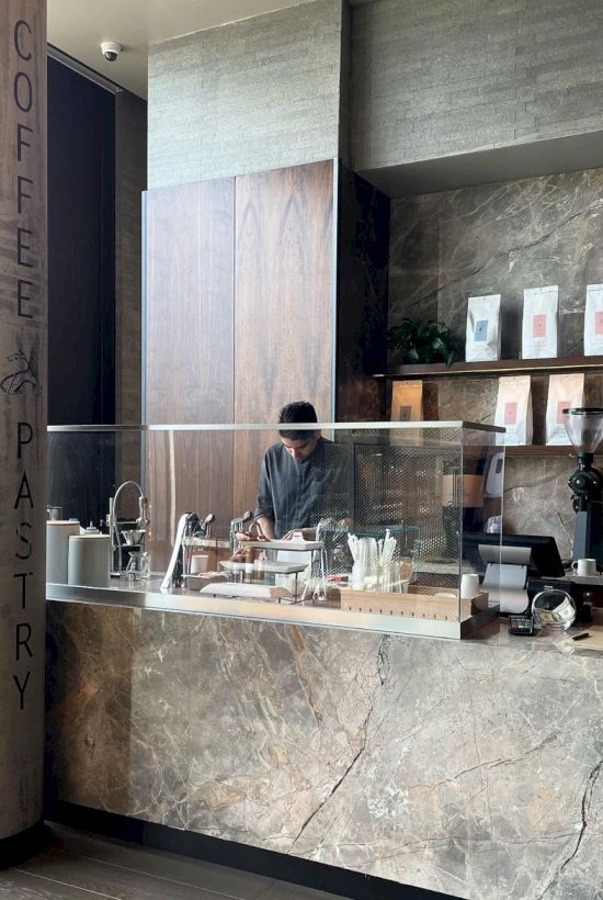 A barista working behind a modern coffee shop counter with a marble finish, glass display, and coffee equipment, labeled as Coffee Pastry.