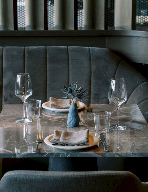 A cozy restaurant booth with a set table, featuring elegant glassware, plates, and napkins on a marble surface.