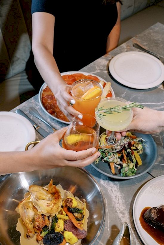 People clinking glasses over a table filled with various dishes, celebrating or dining together in a social setting.