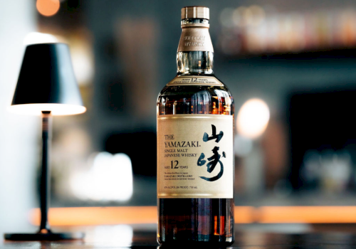 A bottle of The Yamazaki 12-year-old whiskey on a bar counter, with a blurred background and warm lighting.