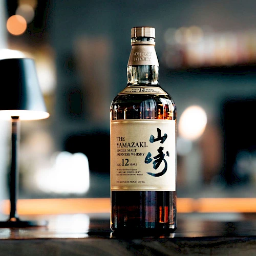 A bottle of The Yamazaki 12-year-old whiskey on a bar counter, with a blurred background and warm lighting.