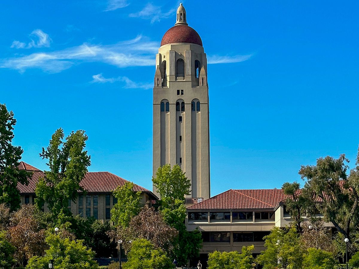 A tall tower with a red dome stands amid greenery and buildings under a clear blue sky, likely part of a university campus.