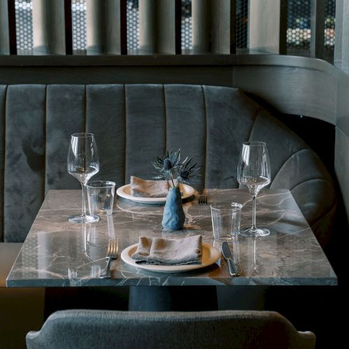 A chic restaurant table setting with plates, wine glasses, and a decorative centerpiece on a marble-topped table with plush seating.