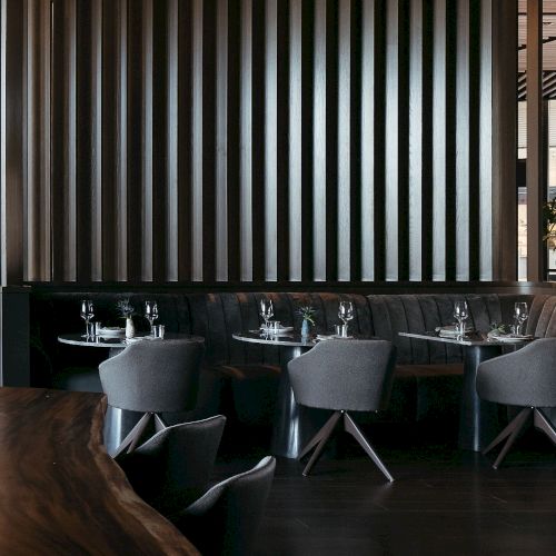 The image shows a modern restaurant interior with sleek tables, gray chairs, and a wooden partition wall.
