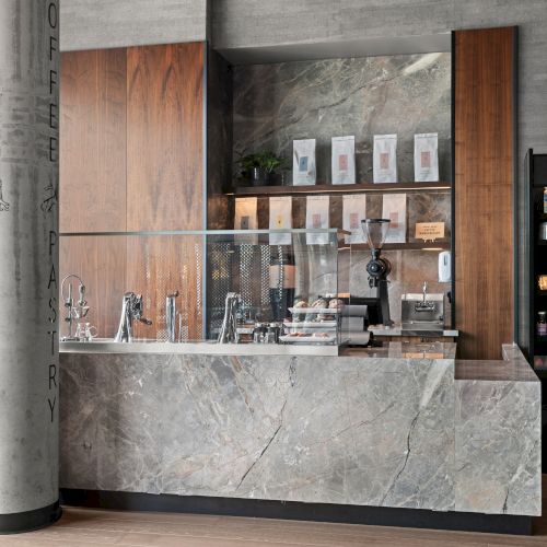 A modern coffee shop counter with coffee machines, packaged goods, and a display fridge filled with drinks and snacks.