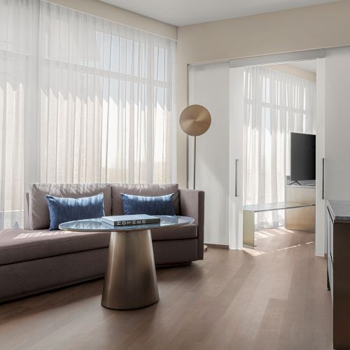 A modern living room with a sofa, round side table, floor lamp, flat-screen TV, and sliding doors, all bathed in natural light from large windows.