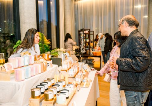 People browsing a market stall with various candles and jars displayed on tables.