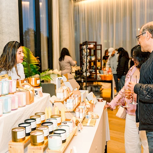 People browsing a market stall with various candles and jars displayed on tables.