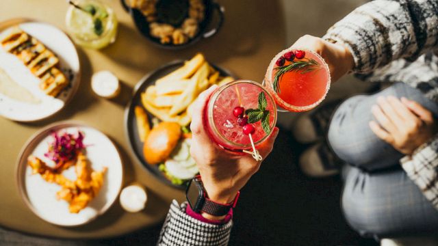 People toasting with red cocktails over a table filled with fries, sliders, and other small dishes, creating a cozy and fun atmosphere.
