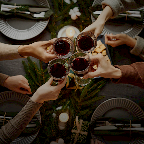 A group of people toasting with glasses of red wine over a festive table setting with greenery and candles.