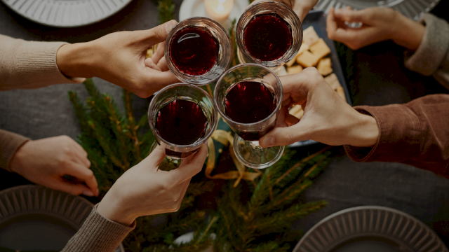 A group of people toasting with glasses of red wine over a festive table setting with greenery and candles.