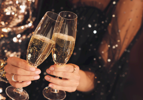 Two people clinking champagne flutes, festive night vibes and sparkling lights.