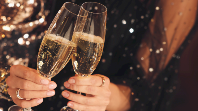 Two people clinking champagne flutes, festive night vibes and sparkling lights.