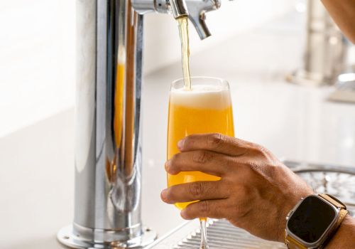 A person pours beer from a tap into a glass, with bowls of pretzels on the counter nearby.