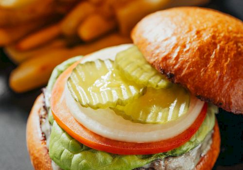 A juicy cheeseburger with lettuce, tomato, onion, pickles, and melted cheese on a toasted bun, served with fries on the side.