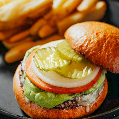 A juicy cheeseburger with lettuce, tomato, onion, pickles, and melted cheese on a toasted bun, served with fries on the side.