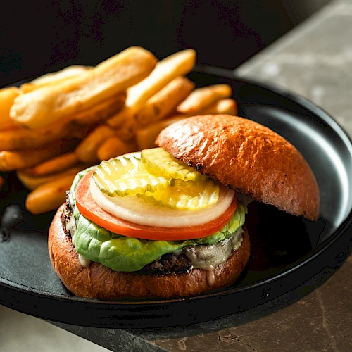A juicy hamburger with lettuce, tomato, onion, pickles, cheese, and a fried egg on a toasted bun, served with crispy french fries alongside.