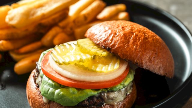 A juicy hamburger with lettuce, tomato, onion, pickles, cheese, and a fried egg on a toasted bun, served with crispy french fries alongside.