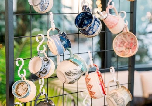 A wall display of many tiny teacups hanging on hooks, upside-down, forming a colorful, whimsical arrangement near a window, decorative and charming.