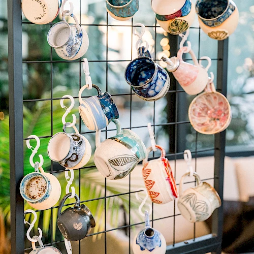 A wall display of many tiny teacups hanging on hooks, upside-down, forming a colorful, whimsical arrangement near a window, decorative and charming.