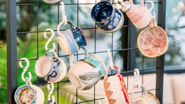 A wall display of many tiny teacups hanging on hooks, upside-down, forming a colorful, whimsical arrangement near a window, decorative and charming.