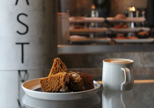 A cafe window with brownies and cookies on a plate beside a cup of coffee, with &ldquo;PAST I&rdquo; lettering on the glass.