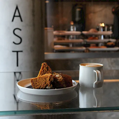 A cafe window with brownies and cookies on a plate beside a cup of coffee, with &ldquo;PAST I&rdquo; lettering on the glass.