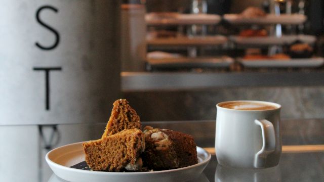 A cafe window with brownies and cookies on a plate beside a cup of coffee, with &ldquo;PAST I&rdquo; lettering on the glass.