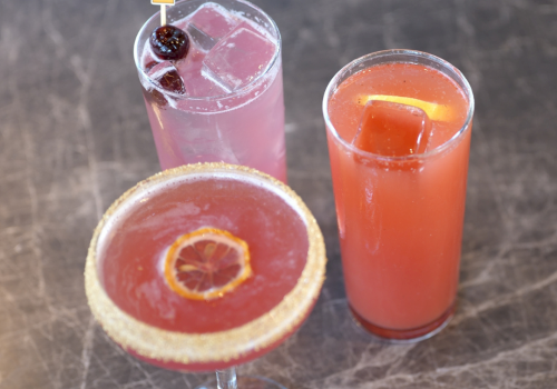 Three colorful cocktails: a pink drink, an orange drink, and a pink drink topped with a &ldquo;Touch Down&rdquo; flag.
