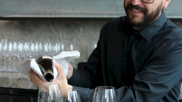 A man pours wine from a bottle into glasses at a tasting table during a presentation.