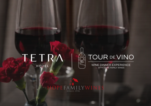 Two filled wine glasses with red wine and flowers, promoting Hope Family Wines&rsquo; &ldquo;Wine Dinner Experience&rdquo; at Hotel.