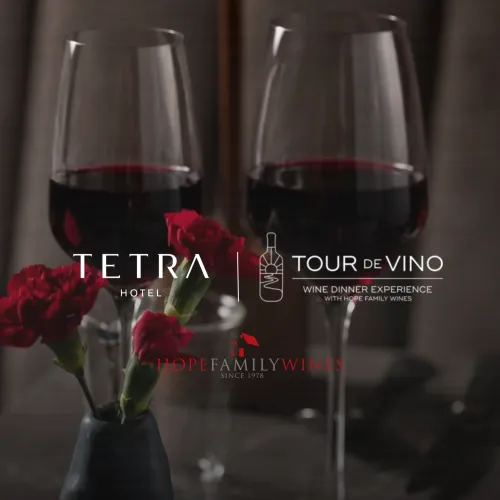 Two filled wine glasses with red wine and flowers, promoting Hope Family Wines&rsquo; &ldquo;Wine Dinner Experience&rdquo; at Hotel.