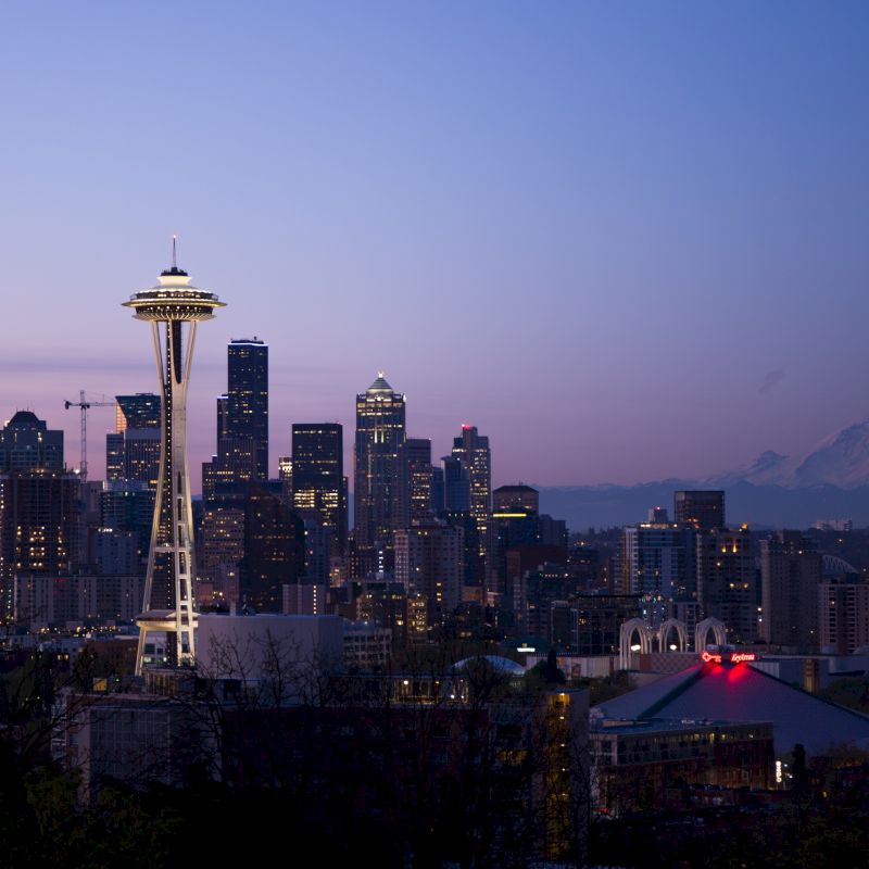 Seattle skyline at dusk with the Space Needle, downtown buildings, and Mount Rainier in the background.